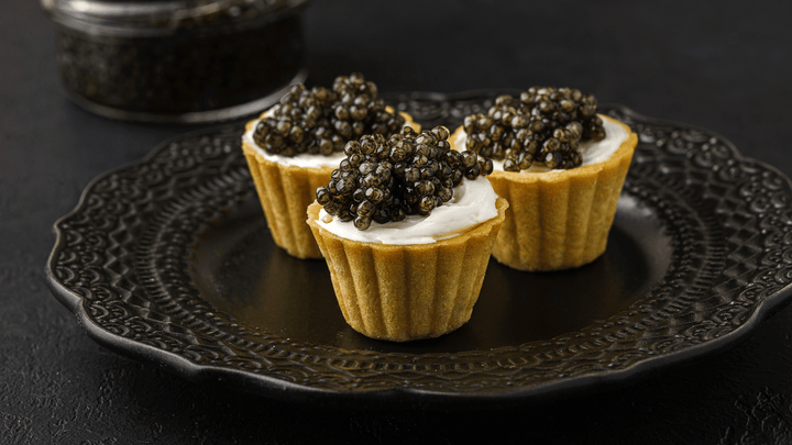 Bowl of cacio e pepe pasta topped with dark caviar on a simple wooden table