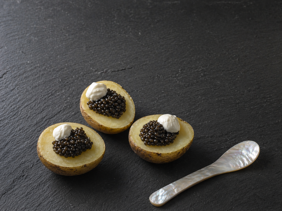 Three small boiled potatoes topped with dark caviar on a dark slate board