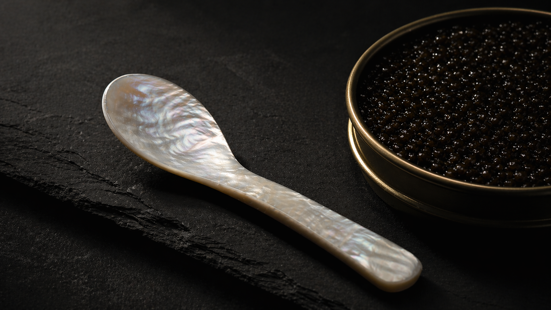 Single mother-of-pearl spoon lying on dark slate beside an open tin of sturgeon caviar
